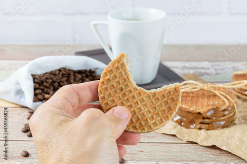 Man holding a stroopwafel with a bite. In the background beans and cup of coffee. photo
