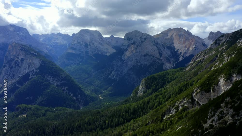 Dolomites, Cortina d'Ampezzo, Veneto, Italy, September 2021. Drone tracks across the densely wooded valley, with a wide vista of rugged mountains touching the clouds in the distance. Dolomites, Cortina d'Ampezzo, Veneto, Italy, September 2021. Drone tracks across the densely wooded valley, with a wide vista of rugged mountains touching the clouds in the distance.