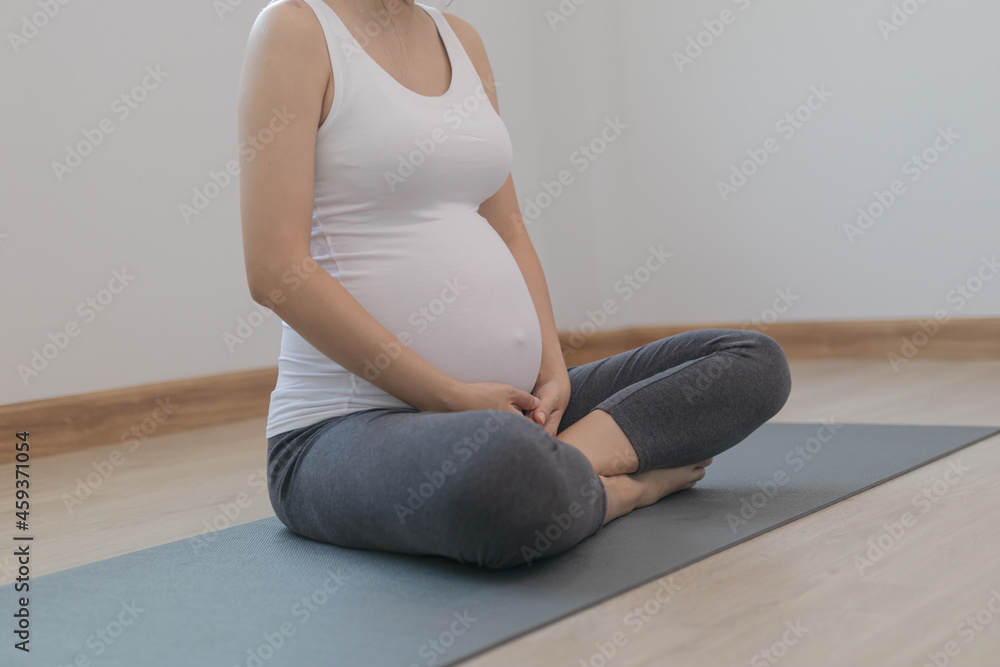 Calm pose asian young pregnant woman practice yoga in the lotus position for pregnant to meditation and exercise on mat for wellbeing while rest at home.