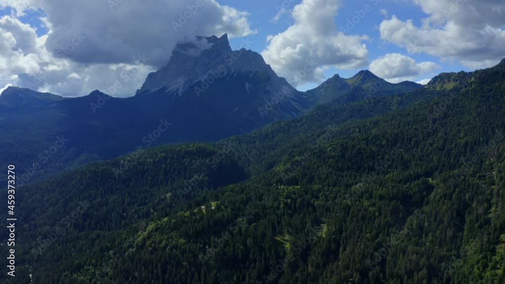 Dolomites, Cortina d'Ampezzo, Veneto, Italy, September 2021. Drone gradually tracks over densely forested hillsides, into the populated valley surrounded by steep mountains reaching into the clouds. Dolomites, Cortina d'Ampezzo, Veneto, Italy, September 2021. Drone gradually tracks over densely forested hillsides, into the populated valley surrounded by steep mountains reaching into the clouds.