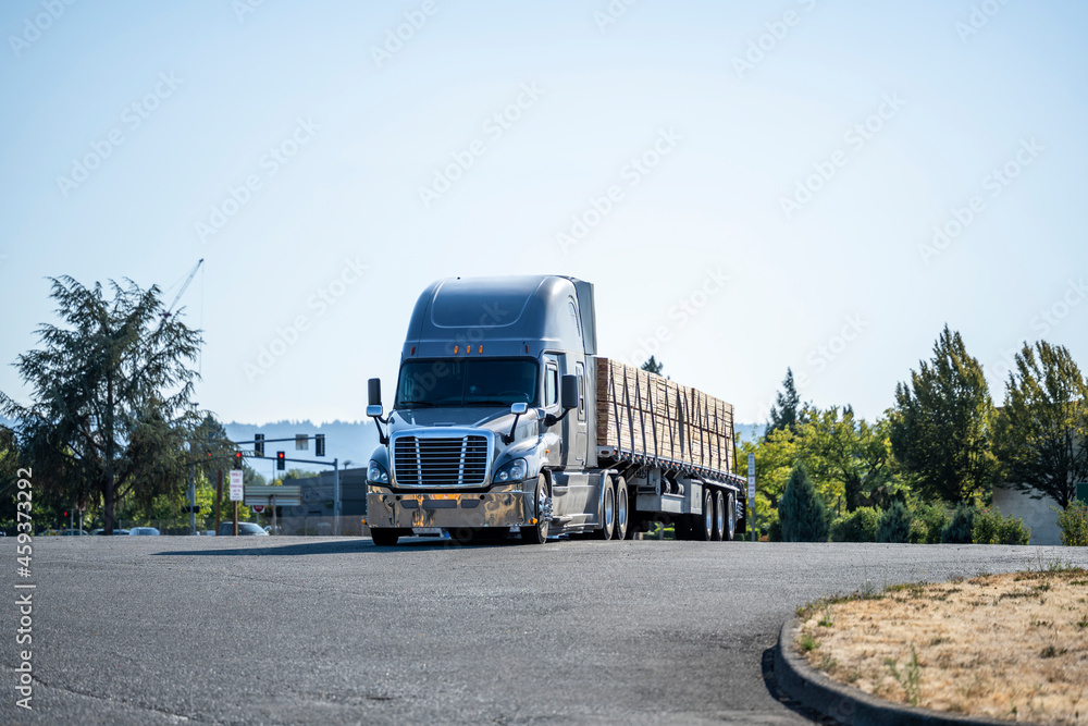 Powerful gray big rig semi truck with loaded by lumber flat bed semi trailer standing on the industrial parking lot take a break