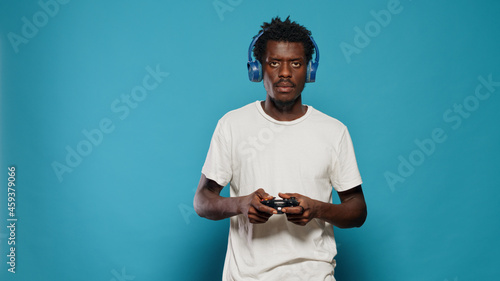 Young man holding joystick to play video games on console. Carefree adult playing online virtual game using controller on television while wearing headphones. Gamer having fun with play © DC Studio