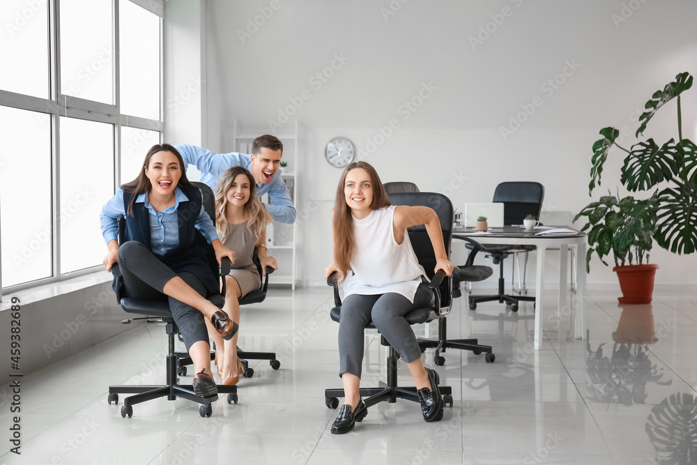 Happy colleagues riding chairs in office