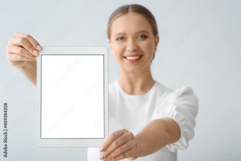 Beautiful young woman holding tablet computer with blank screen on grey background