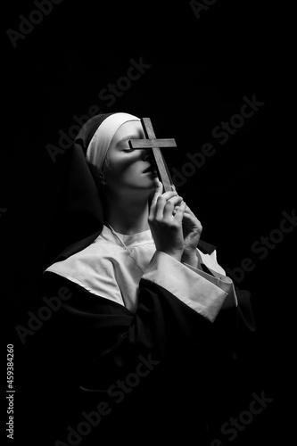 Black and white portrait of young nun with cross on dark background