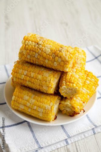 Homemade Butter Parmesan Corn on a white plate on a white wooden background, side view.