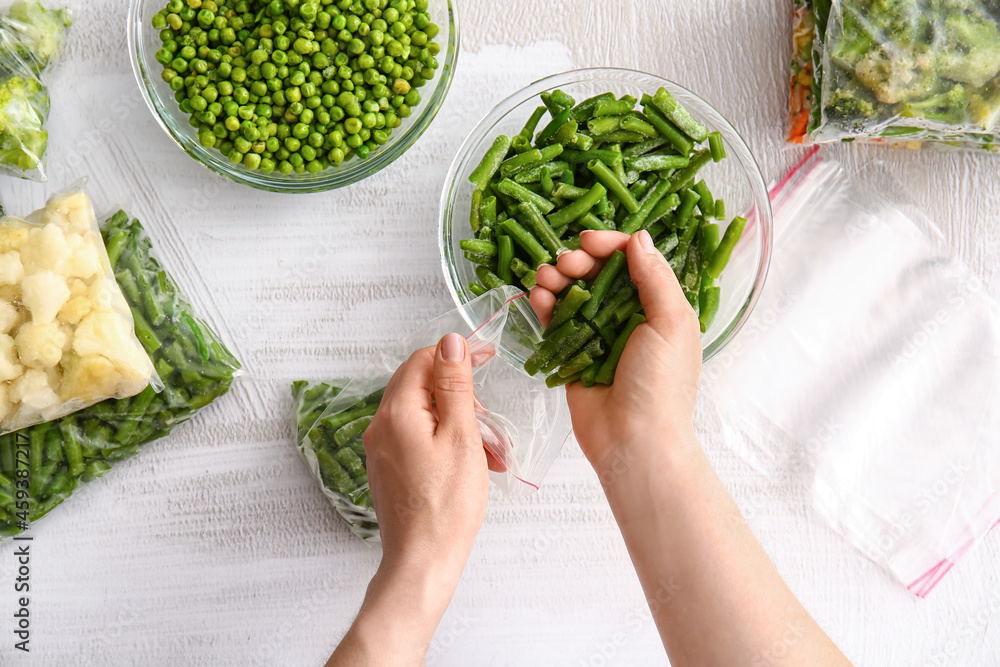 Woman putting frozen green beans in plastic bag on light background