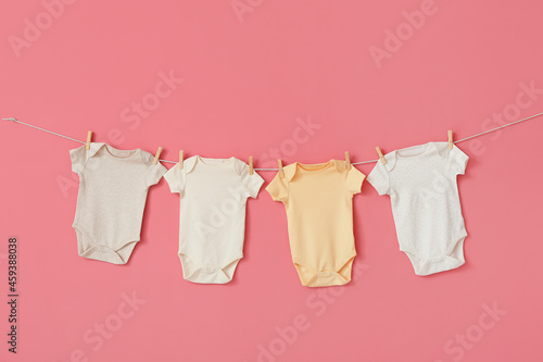 Different baby bodysuits hanging on rope against pink background