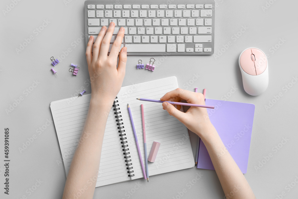 Woman with notebook and keyboard on light background