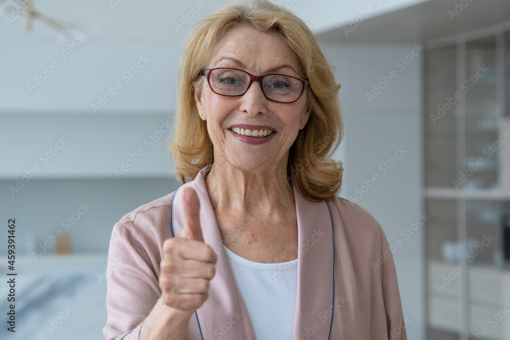 An elderly woman with glasses gives a thumbs up and looks at the camera An elderly woman with glasses gives a thumbs up and looks at the camera
