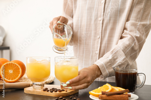 Woman pouring orange juice into glass with ice on light background, closeup