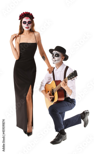 Young couple with painted skull on faces and guitar against white background. Celebration of Mexico's Day of the Dead (El Dia de Muertos)