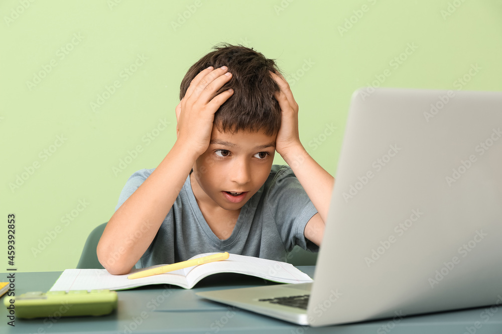 Stressed little boy doing homework at table on color background Stressed little boy doing homework at table on color background