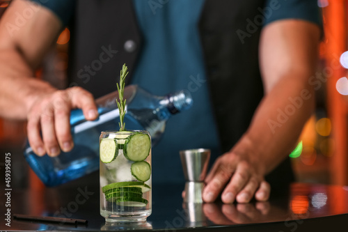 Male bartender making cucumber gin and tonic on table in bar, closeup