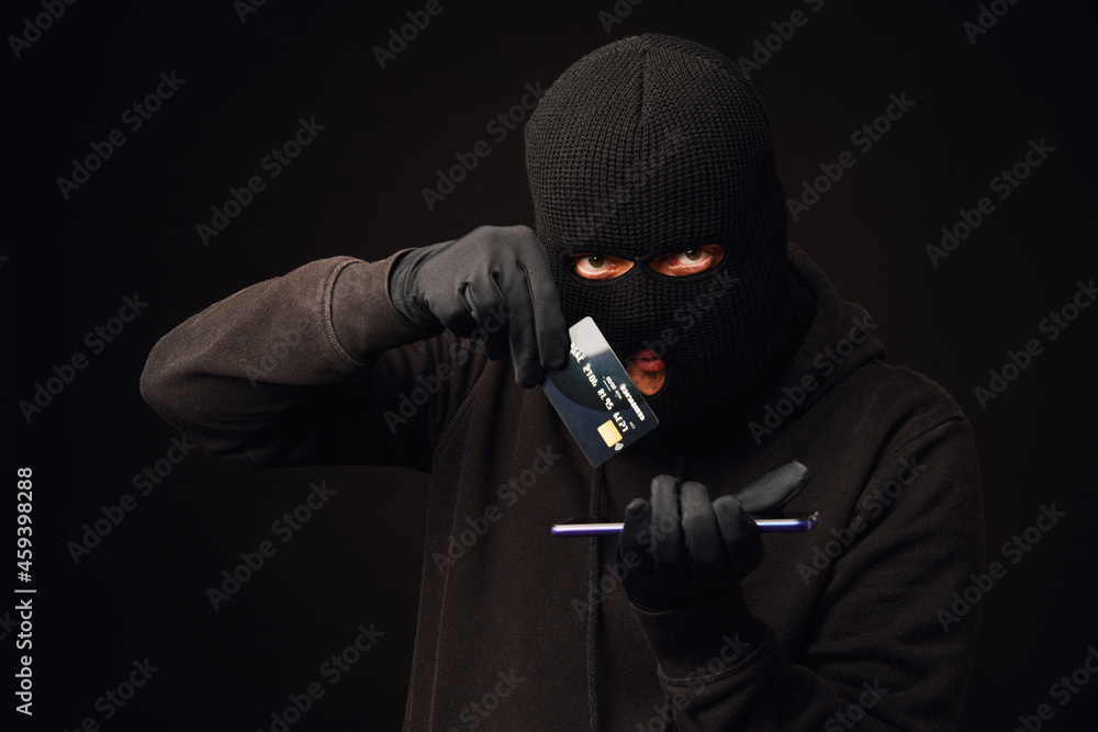Anonymus thief holding credit card and phone. Internet or online banking hacking Anonymus thief holding credit card and phone. Internet or online banking hacking