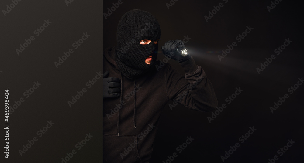 Masked burglar with flashlight on dark back Masked burglar with flashlight on dark back