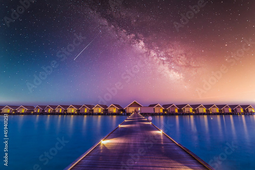 Fototapeta Naklejka Na Ścianę i Meble -  Luxury over water villas, bungalows sea ocean with beach at night sunset time, Milky Way. Exotic adventure carefree travel vacation, summer resort landscape. Fantasy nature resort hotel landscape