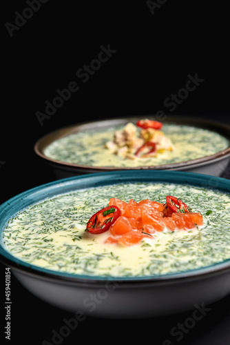 Summer cold yogurt soup okroshka with salmon served in a blue bowl over black background. photo