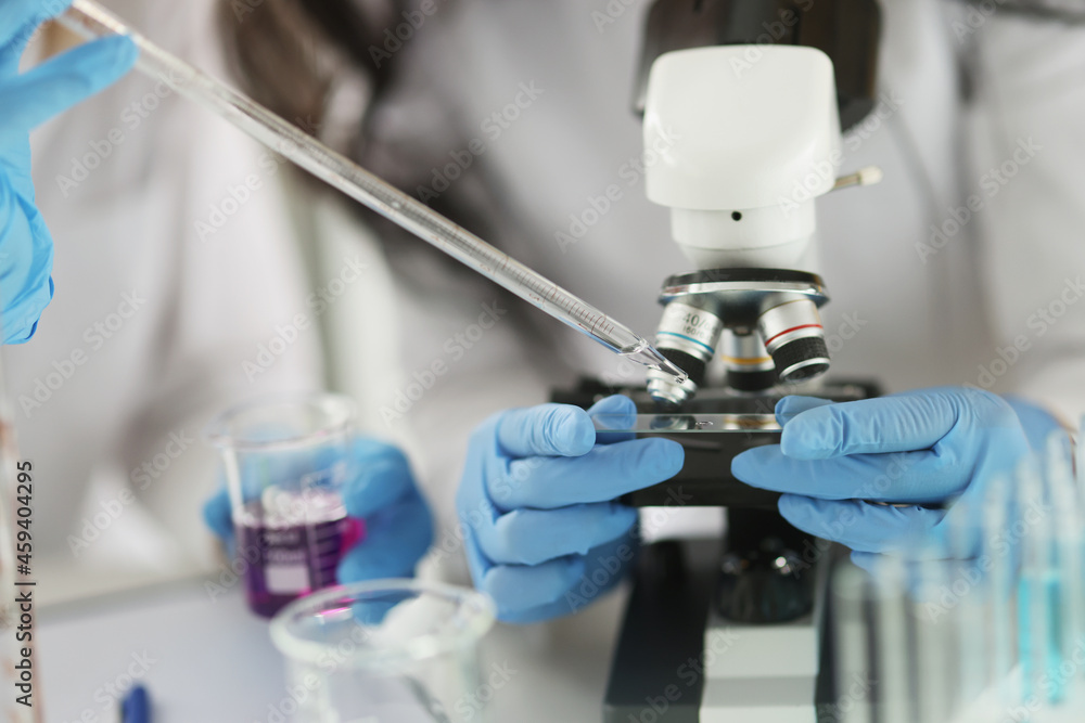 Scientist in gloves conducts laboratory studies of liquid on microscope Scientist in gloves conducts laboratory studies of liquid on microscope