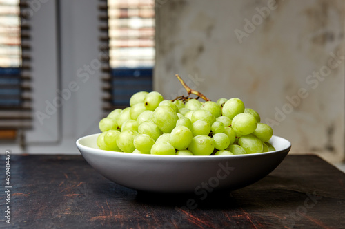 Branch of ripe green grape on plate. Juicy grapes on wooden background, closeup. Grapes on dark kitchen table with copy space