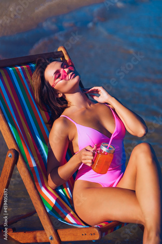 Attractive redhead girl on a deckchair sunbathing near the sea with a glass of juice in her hand