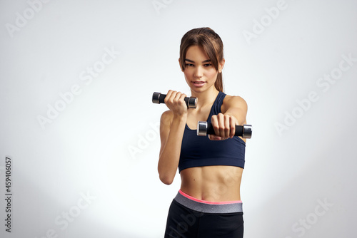 pretty woman fitness exercise dumbbells in the hands of Strong light background