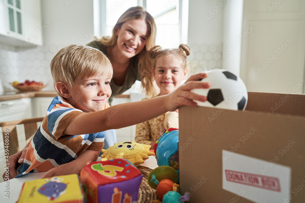 Smiling boy putting toy in donation box with family in background at home Smiling boy putting toy in donation box with family in background at home