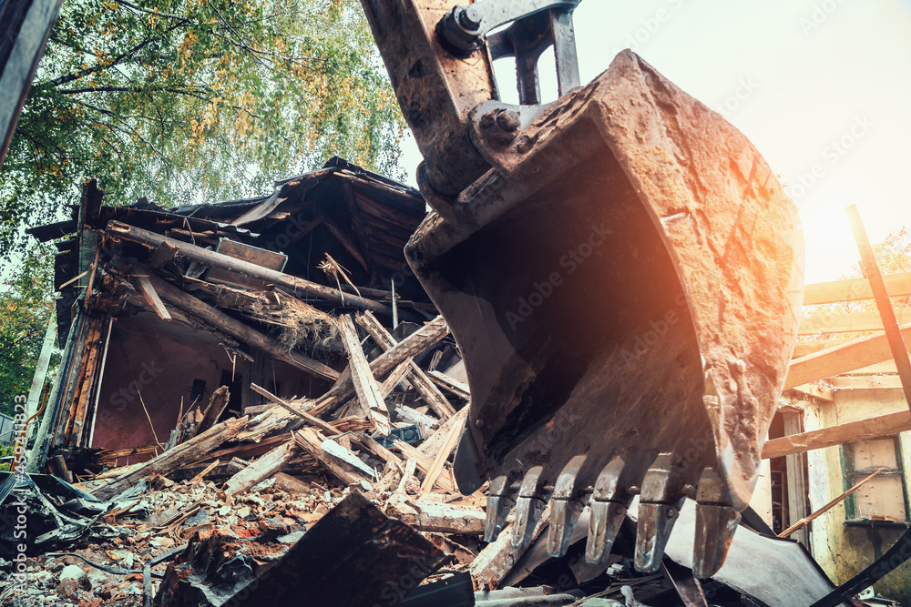Fototapeta premium Demolition building construction concept. Excavator shovel or bucket at background of debris broken house.
