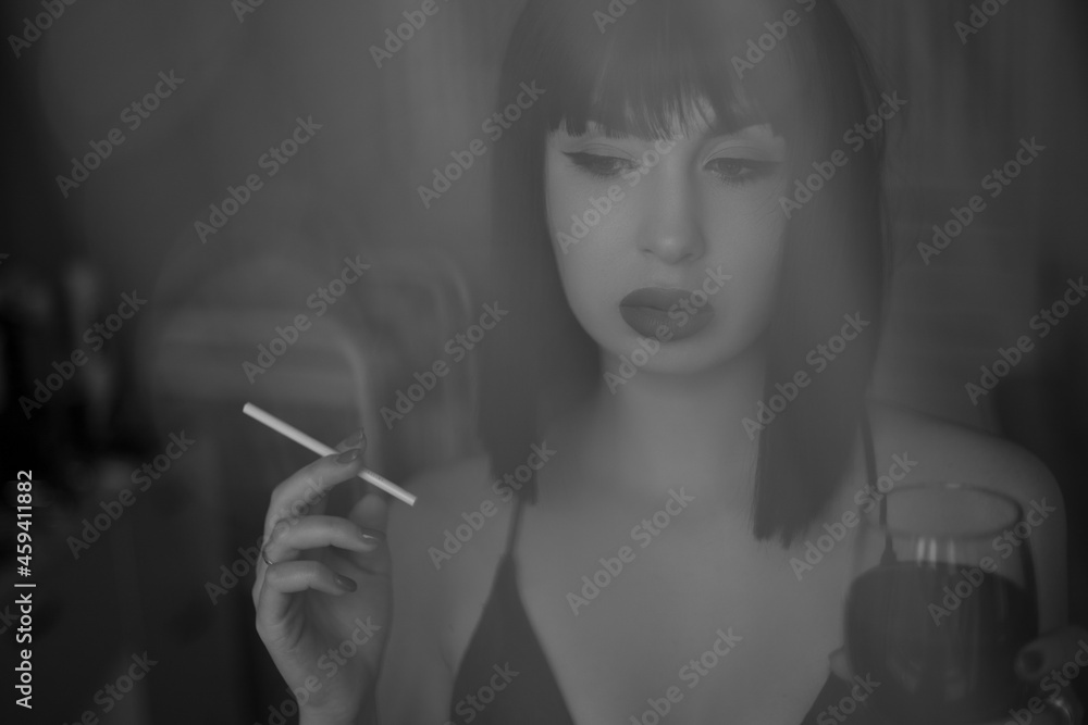 Fototapeta premium Young beautiful woman in a black wig, like Cleoparta with glass of wine and cigarette, a little pensive and sad. Black and white photography. Close up portrait. Soft photography.