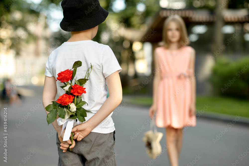 Fototapeta premium Children's date, boy hides flowers from a girl