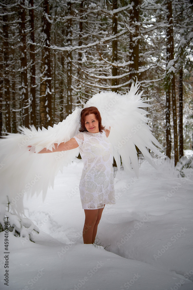 Woman looking as fairy angel with wings with white feathers in the forest with snow and snowdrifts on cold winter day Woman looking as fairy angel with wings with white feathers in the forest with snow and snowdrifts on cold winter day