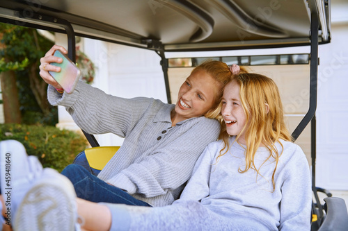Happy girls taking selfie while sitting in golf cart