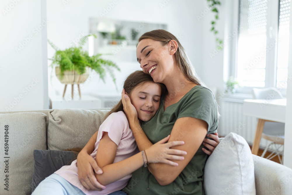 Close up of sweet pretty daughter cuddling with her young mother. Lovely mother embracing her cute daughter on the sofa at home. Close up of sweet pretty daughter cuddling with her young mother. Lovely mother embracing her cute daughter on the sofa at home.