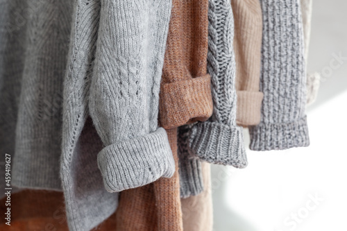 Pastel warm knitted clothes sweater hanging in the closet. Cozy autumn and winter wardrobe. photo