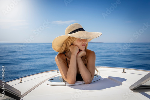 Foto A beautiful, blonde woman with sunhat enjoys the summer sun on a boat over calm