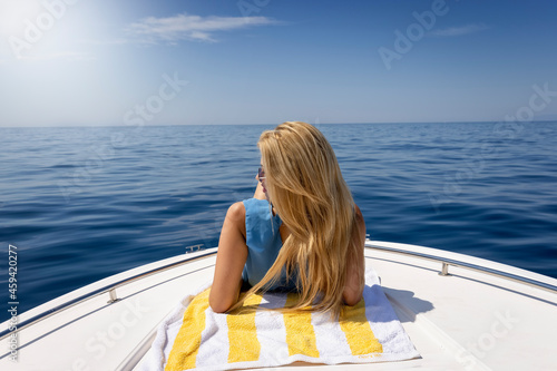 A blonde woman relaxes under the summer sun on a boat over calm sea
