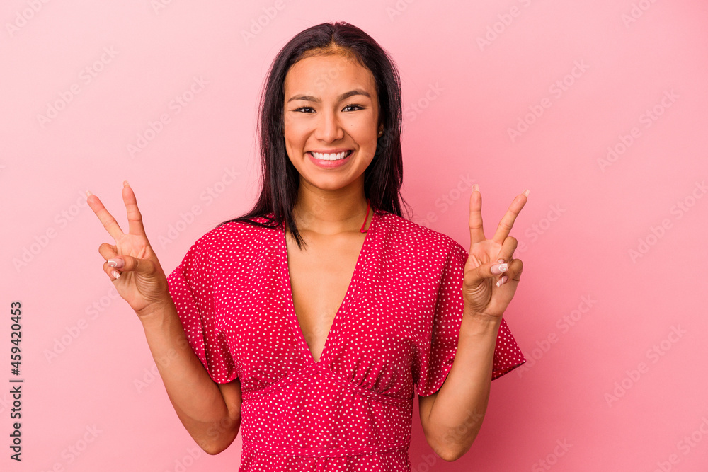 Young latin woman isolated on pink background showing victory sign and smiling broadly. Young latin woman isolated on pink background showing victory sign and smiling broadly.