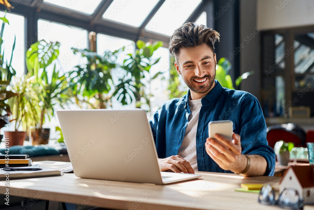 Smiling male professional using mobile phone while sitting at desk in office Smiling male professional using mobile phone while sitting at desk in office