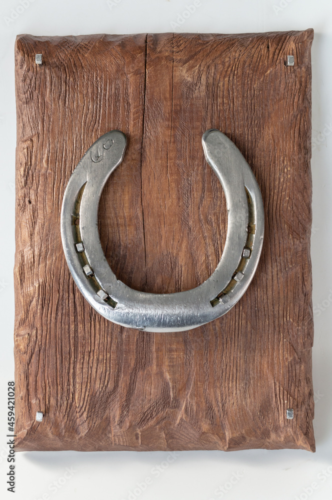 A shiny metal horseshoe, nailed with forged nails to a painted matte board. A souvenir for storing keys. On a light background. A shiny metal horseshoe, nailed with forged nails to a painted matte board. A souvenir for storing keys. On a light background.