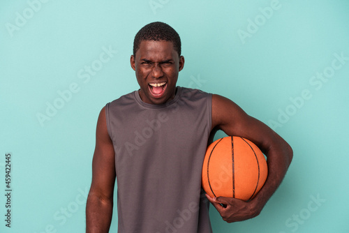 Young African American man playing basketball isolated on blue background screaming very angry and aggressive.