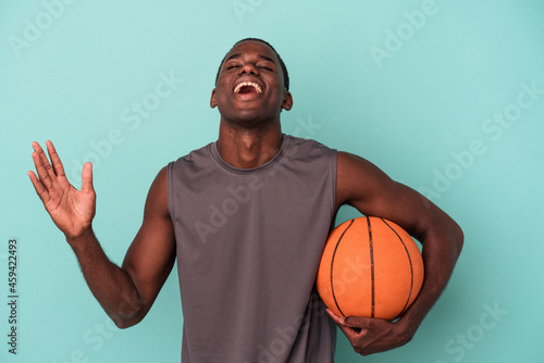Young African American man playing basketball isolated on blue background receiving a pleasant surprise, excited and raising hands. © Asier