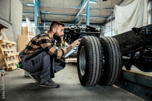 An auto-mechanic crouching next to a tire with a tablet in his hands and checking on it. Worker in the auto-mechanic workshop © dusanpetkovic1