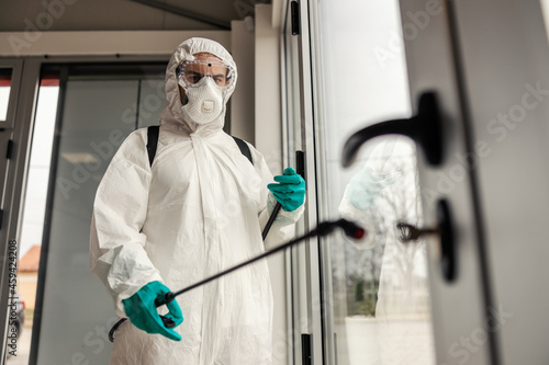 Coronavirus outbreak situation. A male specialist in a special protective suit and sprayer refreshes and cleans the door and windows. Social distancing,keep distance in public to protect from COVID-19