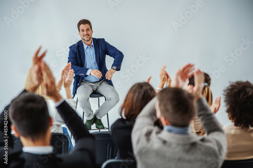 Murais de parede Smiling motivational speaker sitting in front of his audience who is clapping