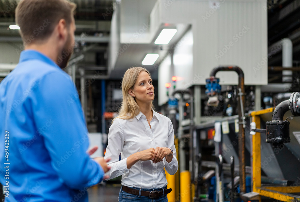 Businesswoman checking machine while standing with coworker in factory Businesswoman checking machine while standing with coworker in factory