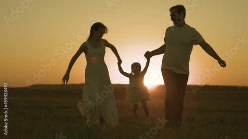 Happy father and mother run across field with small child sunset in sky, silhouette cheerful family, childhood dream of parents, play together, give attention to children, love of mom and dad for kid