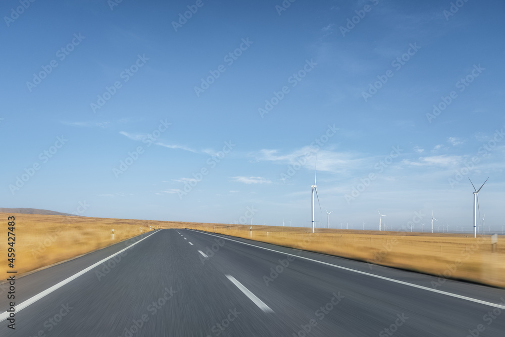 empty road through grassland view and wind farm