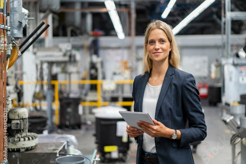 Young blond female manager holding digital tablet at industry photo