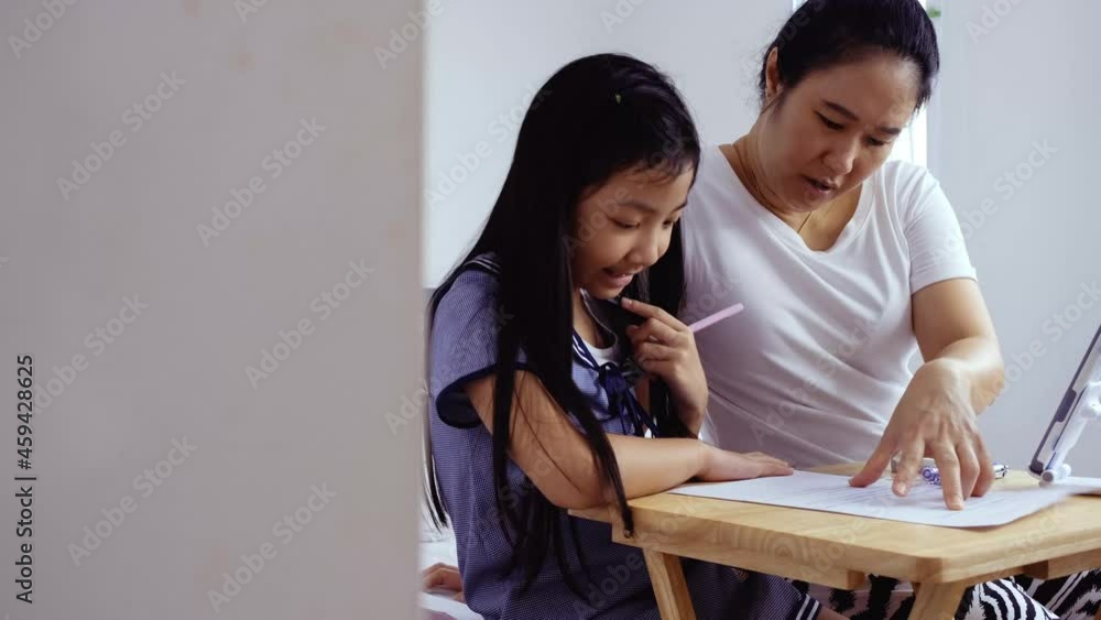Mother is teaching homework to Asian daughter who is homeschooled during the COVID-19 pandemic with love and warmth. Mother is teaching homework to Asian daughter who is homeschooled during the COVID-19 pandemic with love and warmth.