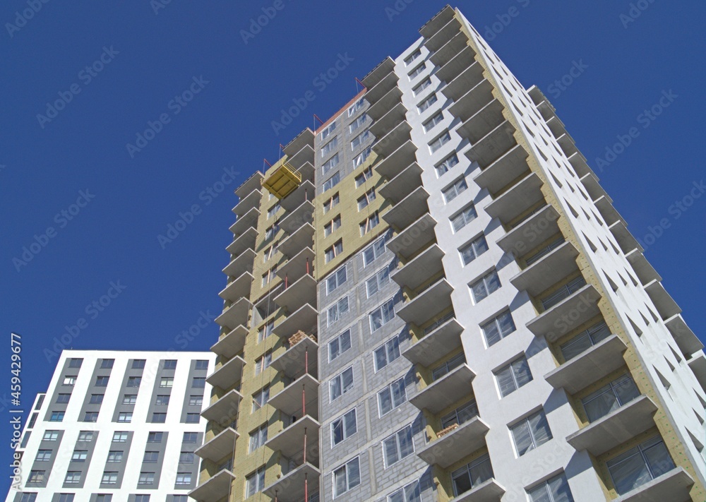Construction of a multi-storey residential building. Installation of insulation on external walls. A house under construction, a newly built house, blue sky.